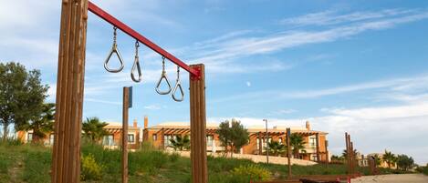 A beach with a wooden swing set, a bench, and a building in the background.