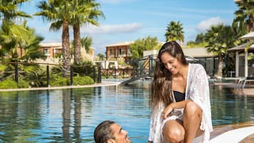 Zona de piscina con palmeras y edificios al fondo.