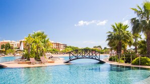 Una piscina con un puente, palmeras y sillas de descanso.