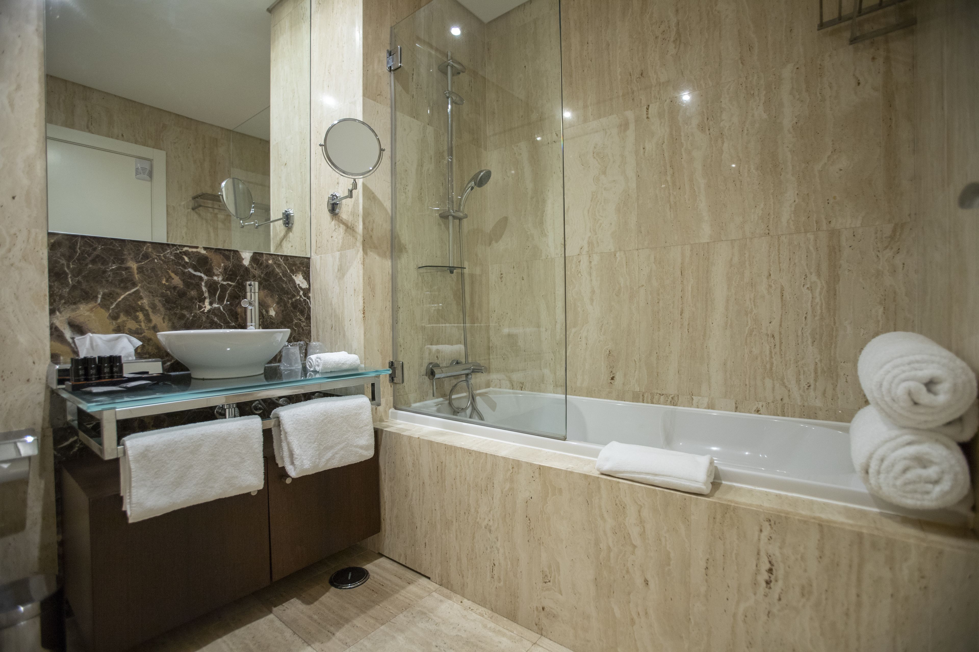 A modern bathroom with a glass-enclosed shower, a large bathtub, and a marble vanity with a sink and towel rack.