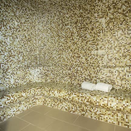 A mosaic-tiled room with a bench and a rolled towel.