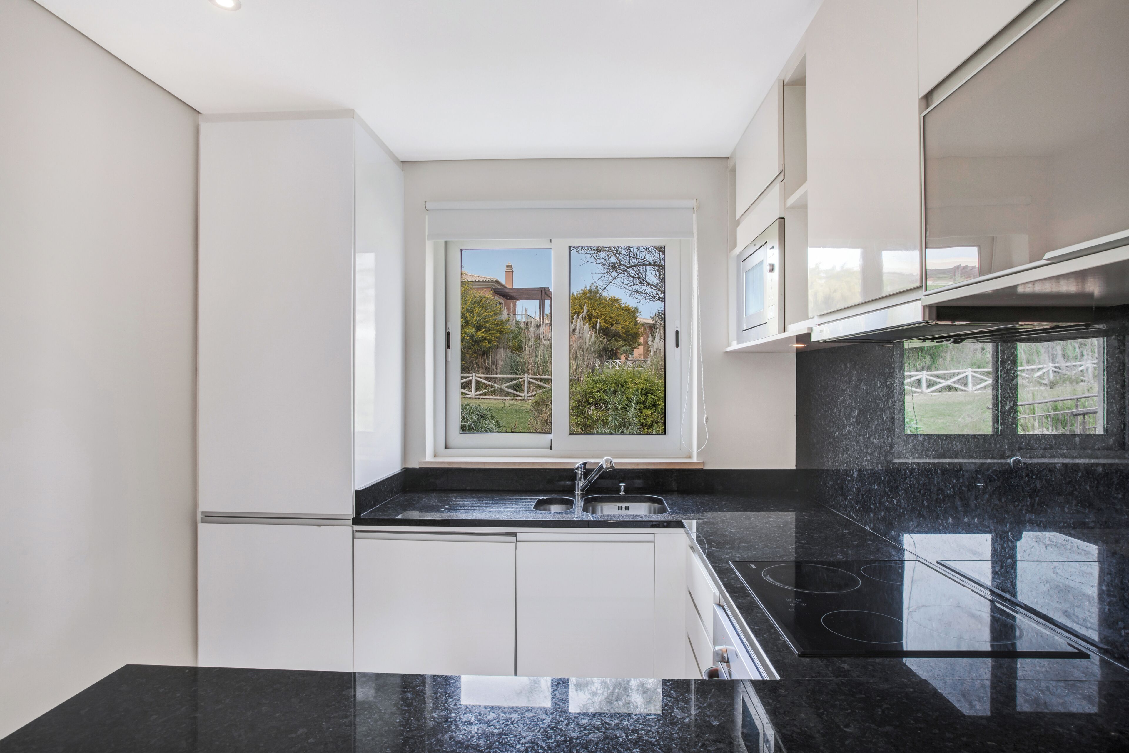 Een moderne keuken met een zwart granieten aanrecht, witte kasten en een raam met uitzicht op de omgeving.