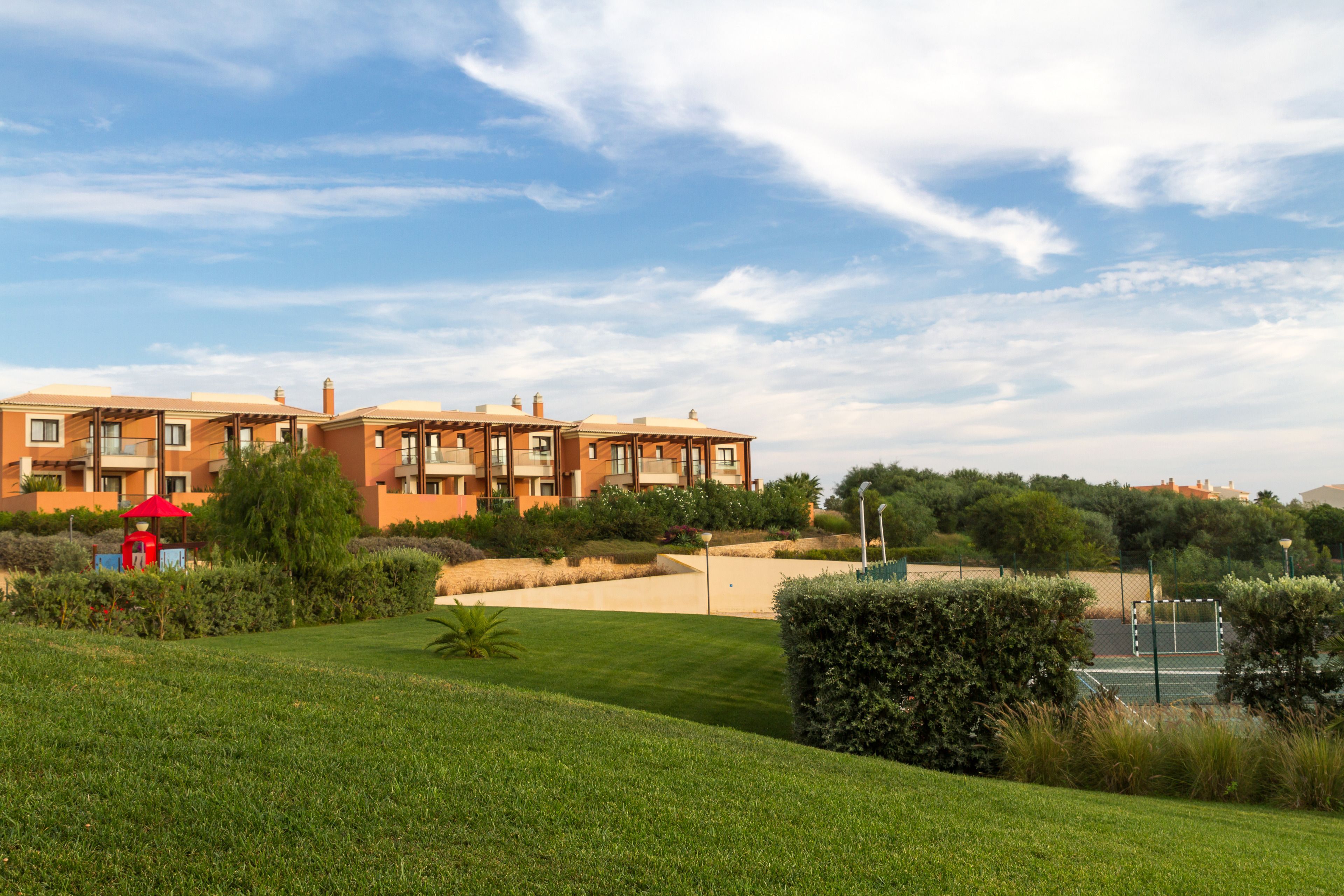 A residential building with multiple balconies, a well-maintained lawn, and a tennis court.