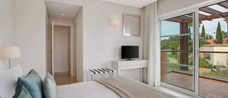 A hotel room with a bed, a TV, a desk, and a balcony with a view of greenery.