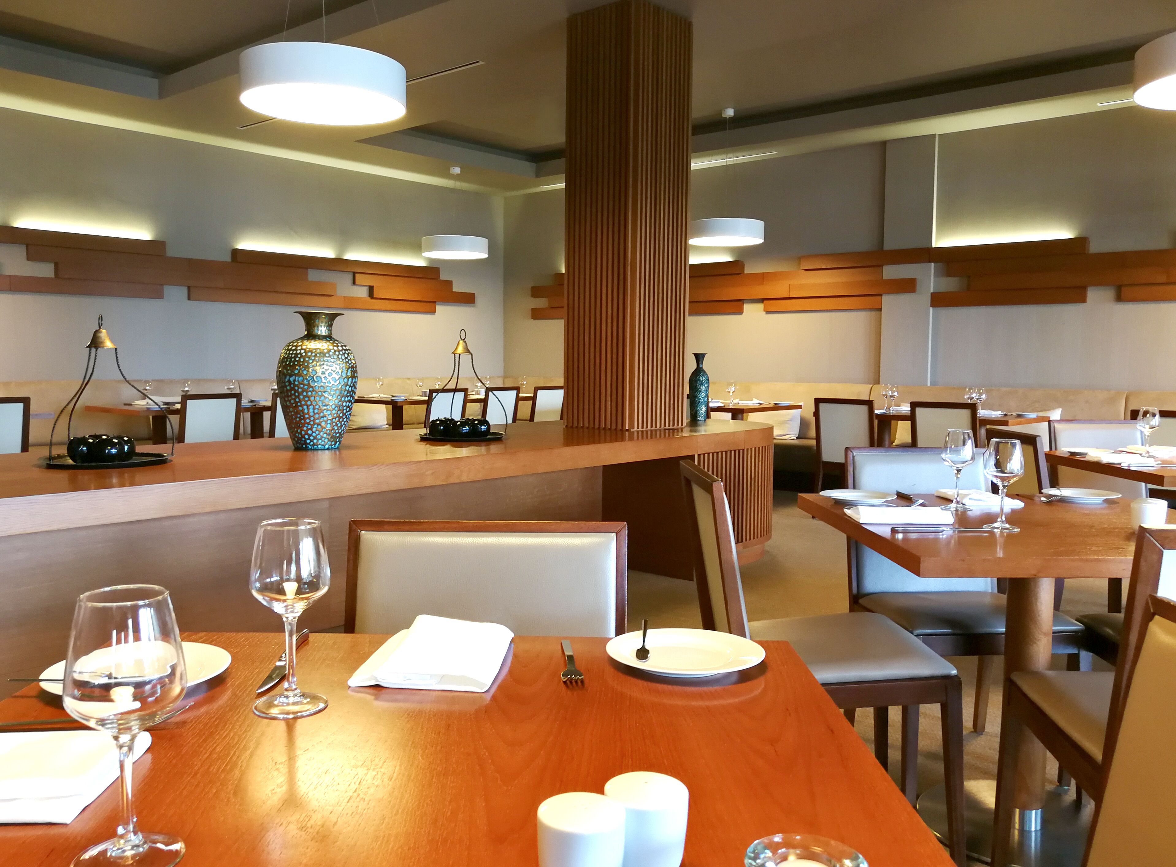 En restaurang med bord och stolar i trä, en central pelare och hängande taklampor.