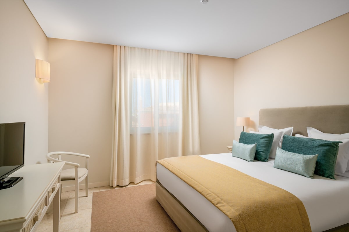 A hotel room with a bed, a desk, a chair, and a TV.