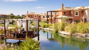 Un resort con un canal de agua, muelle de madera con cortinas blancas y edificios con techos de teja.