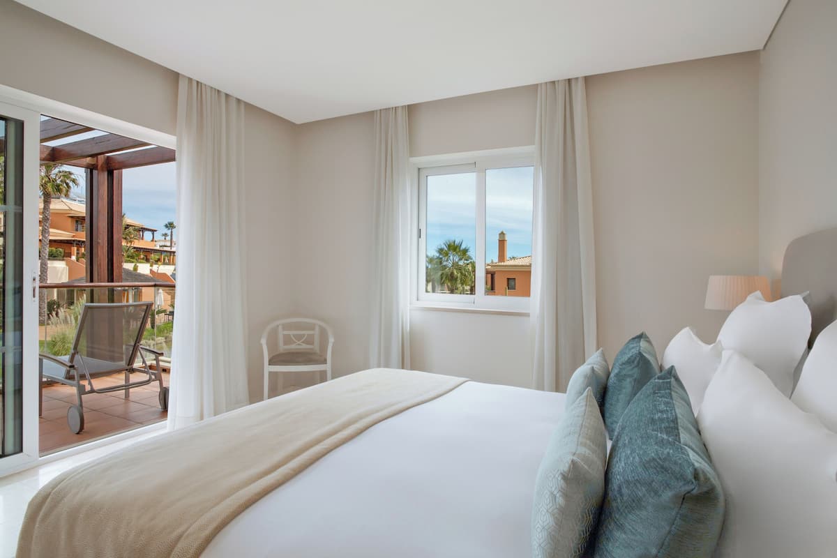 A hotel room with a bed, a window with curtains, a chair, and a view of the outside.