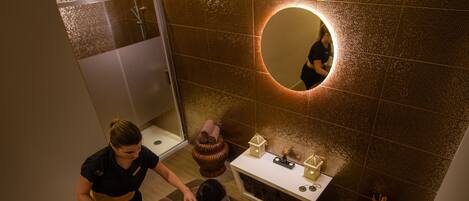 A spa room with a massage table, a mirror, a small table with candles, and a decorative bowl.