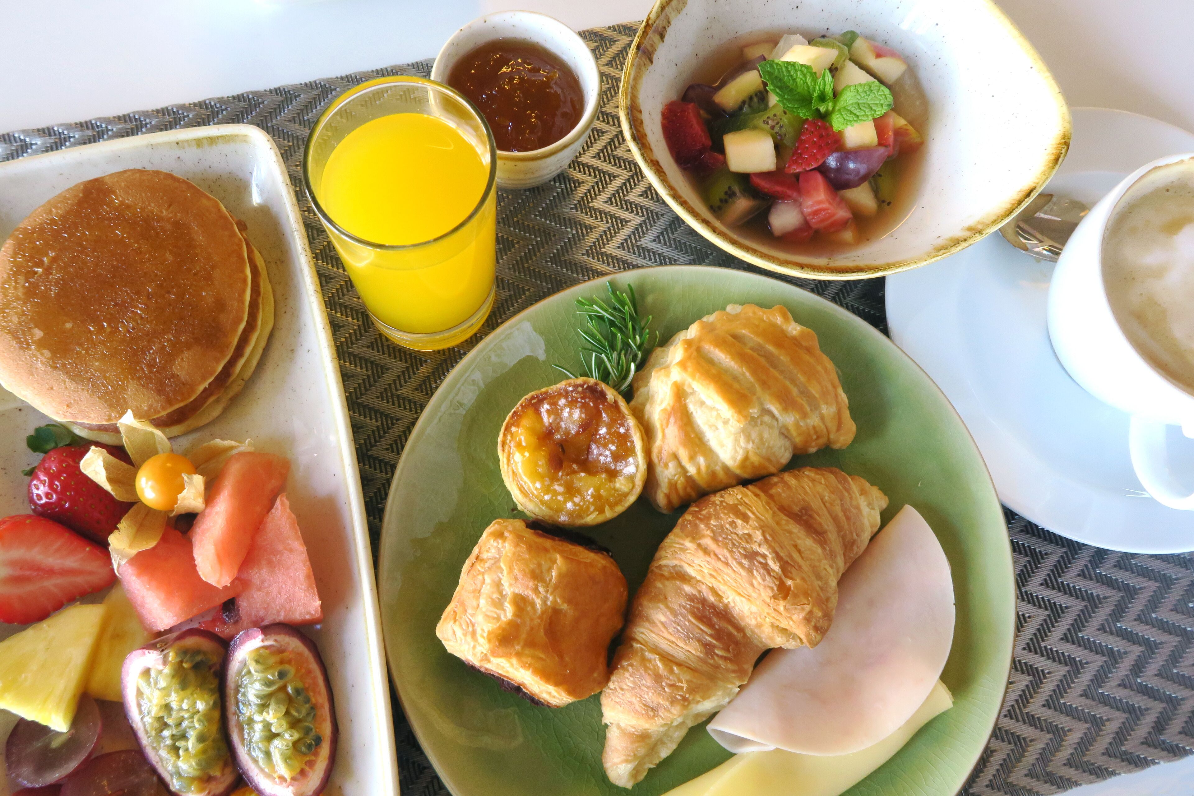 A breakfast plate with pancakes, croissants, and a fruit salad.