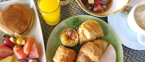 A breakfast plate with pancakes, croissants, and a fruit salad.