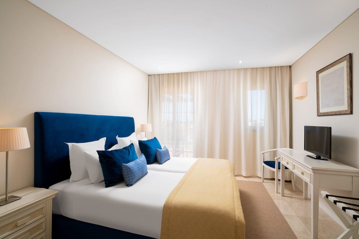 A hotel room with a large bed, a desk, a chair, a television, and a window with curtains.