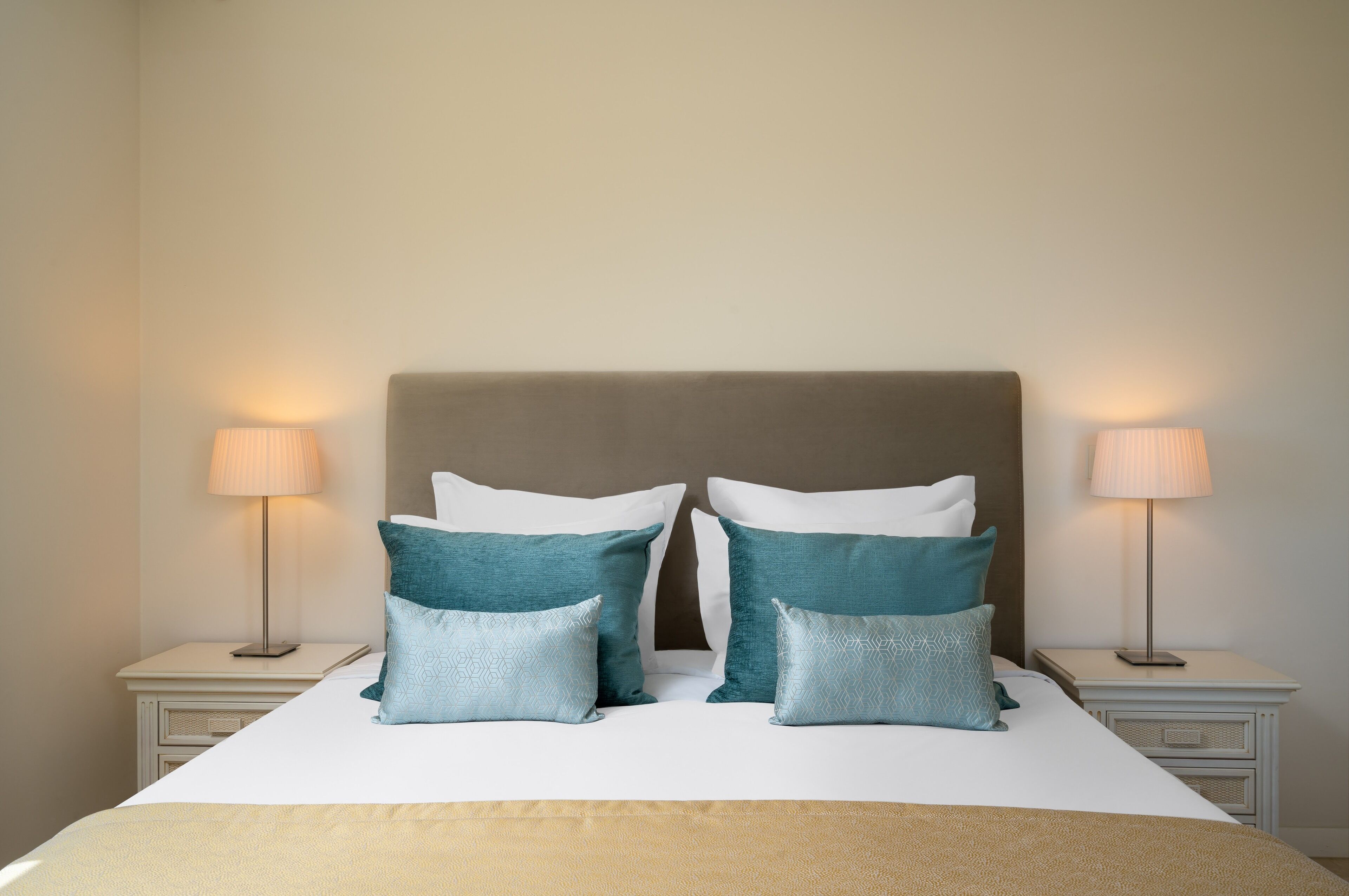 A neatly made bed with a headboard, two bedside tables with lamps, and decorative pillows.