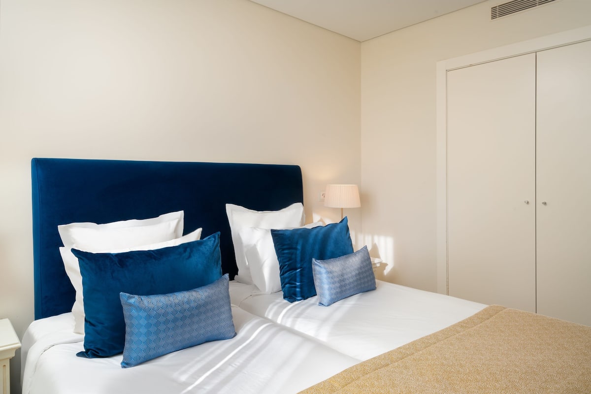 A neatly made bed with a blue headboard, white bedding, and several blue pillows.
