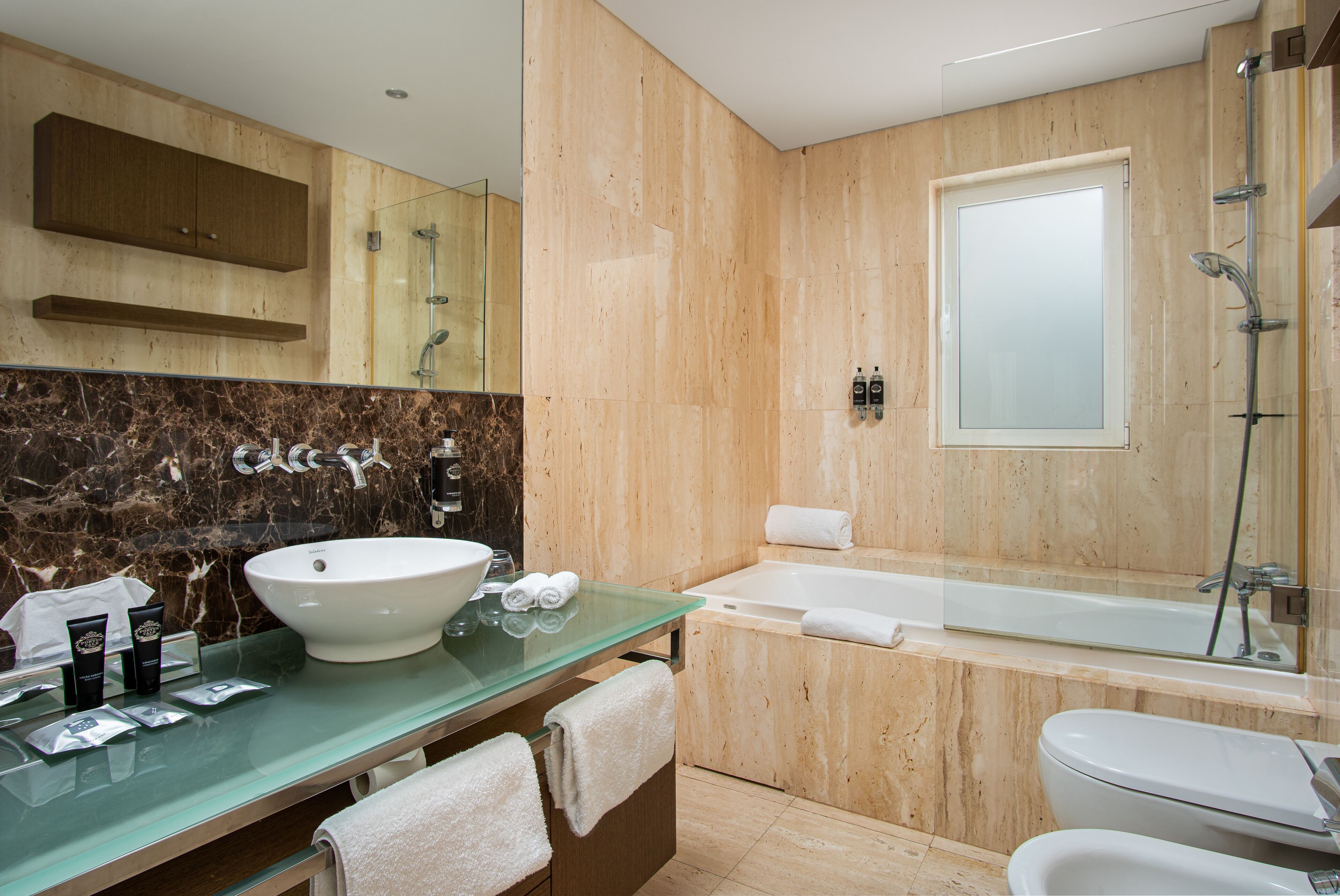 A modern bathroom with a glass vanity, a large white sink, a bathtub, and a toilet.