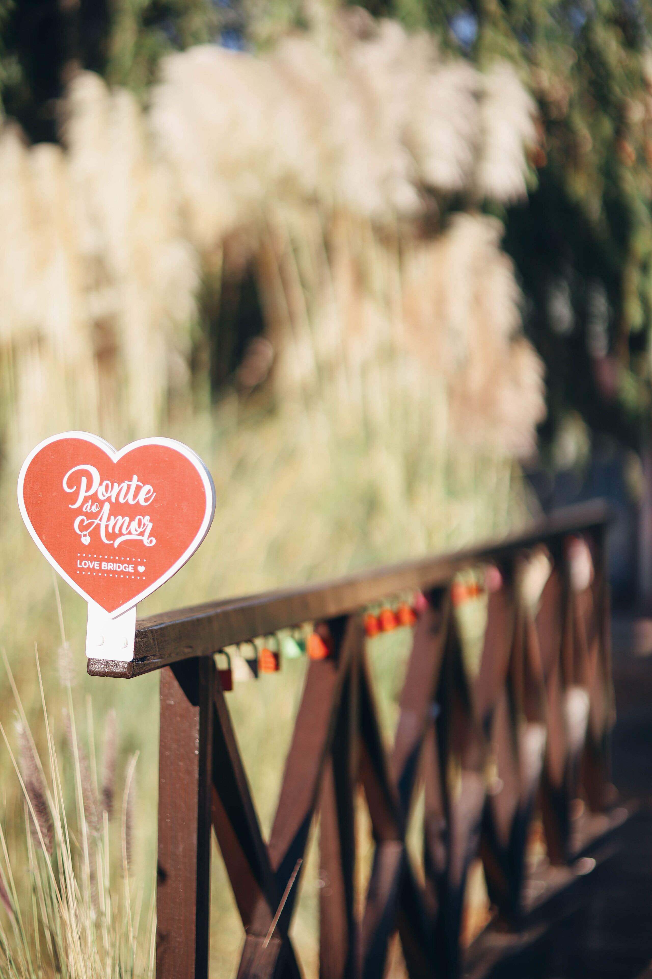 Une plaque en forme de cœur portant les inscriptions « Ponte do Amor » et « Love Bridge », fixée à la rambarde d’un pont en bois.