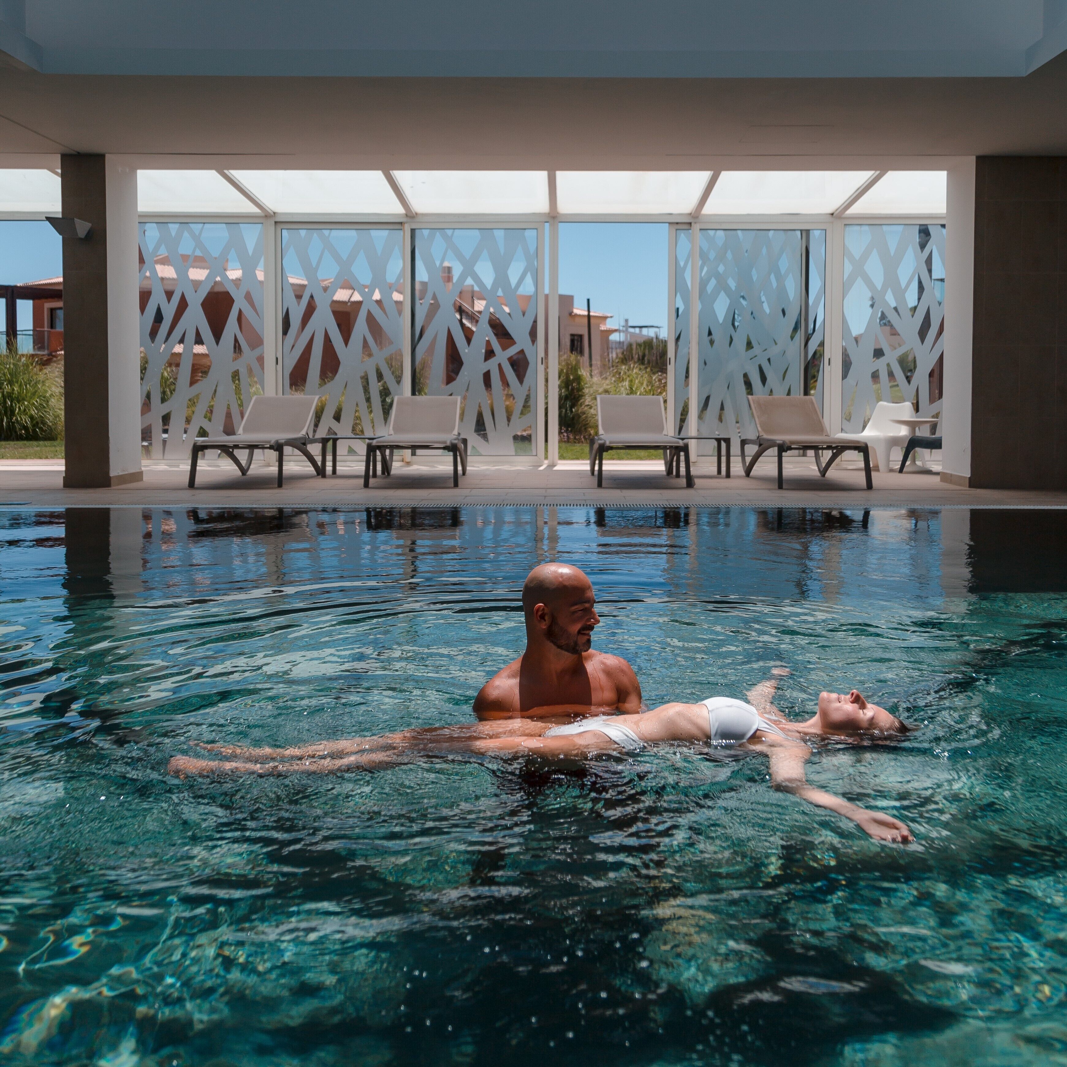 A swimming pool with clear water, surrounded by white lattice panels and lounge chairs.