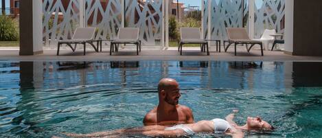 A swimming pool with clear water, surrounded by white lattice panels and lounge chairs.