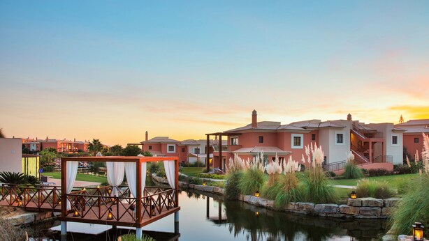 Un resort con fuente de agua, un área de estar techada y una hilera de casas con vista al atardecer.