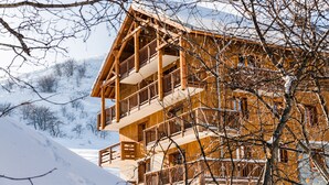 Una cabaña de madera de varios pisos con balcones, con montañas nevadas como telón de fondo.