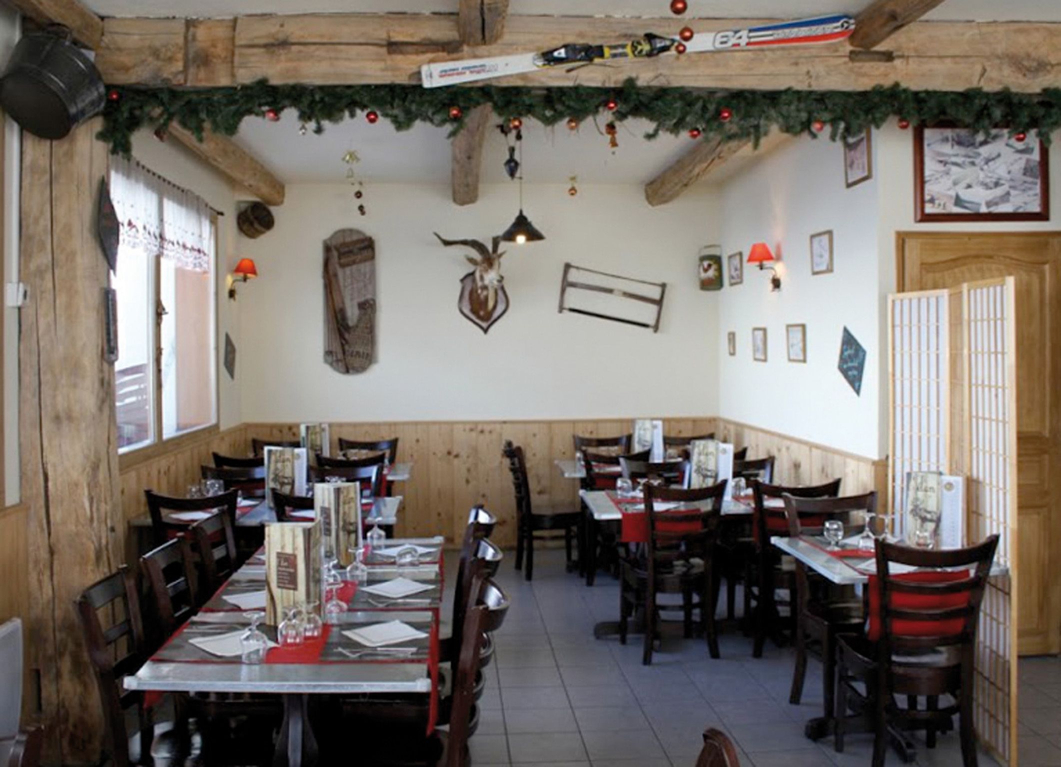 Een restaurant met houten wanden en plafond, versierd met kerstkransen en decoraties. Tafels zijn gedekt met menukaarten en glazen.