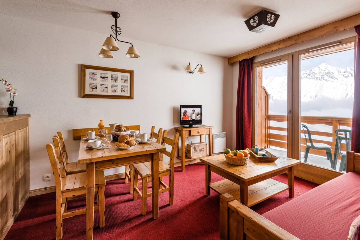 Una habitación acogedora con una mesa de madera, sillas, un televisor y una ventana con vistas a la montaña.