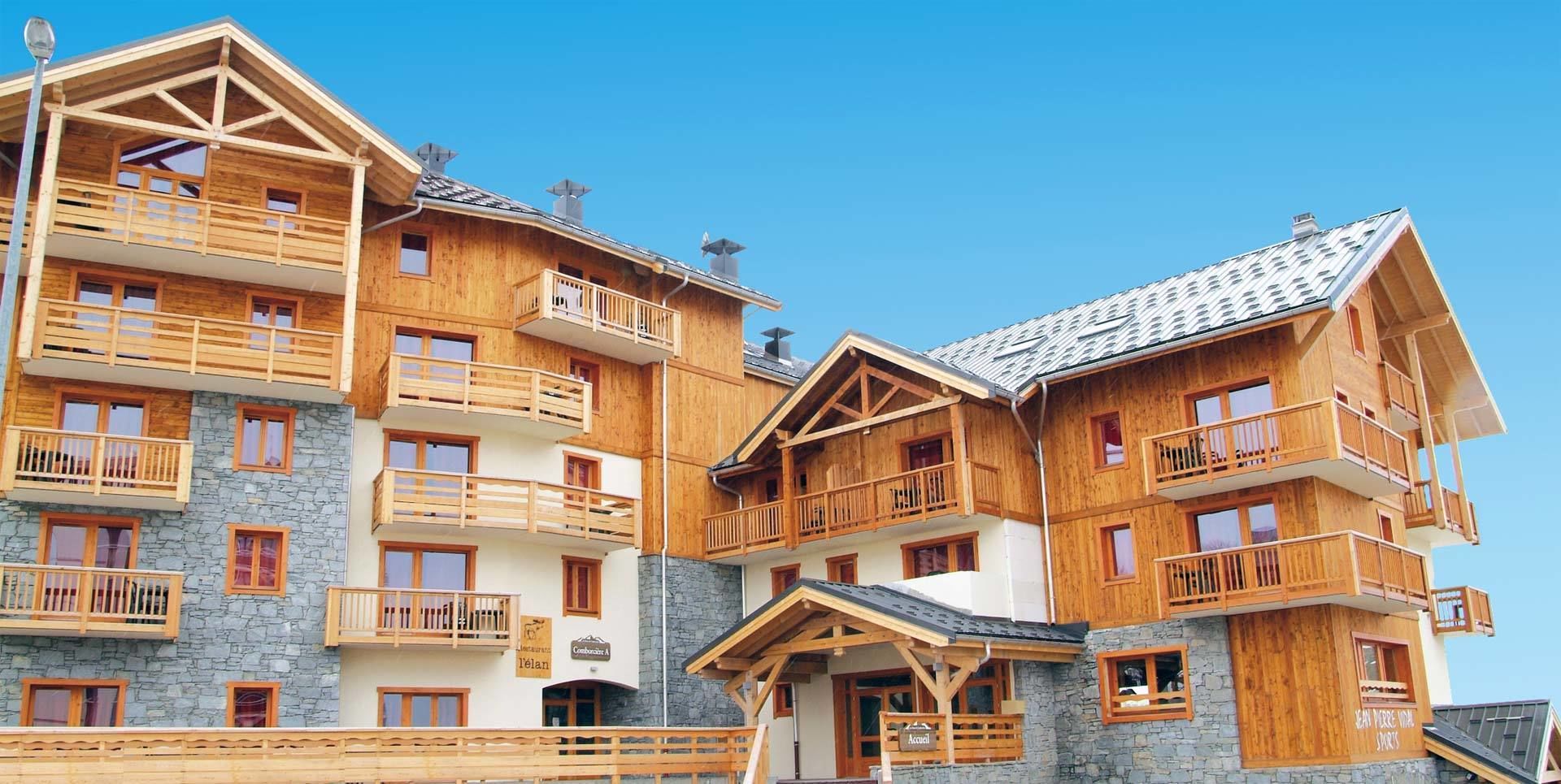 Un bâtiment en bois à plusieurs étages, doté de balcons et de murs en pierre, qui ressemble probablement à un hôtel ou à un complexe touristique.