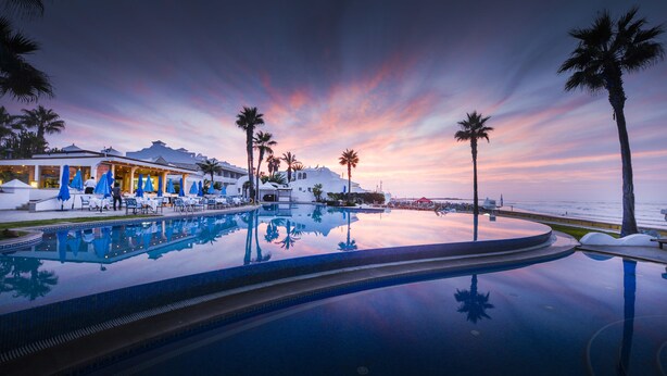 A resort pool with palm trees and a sunset view. - L'amphitrite Palace Resort & Spa (Skhirat)
