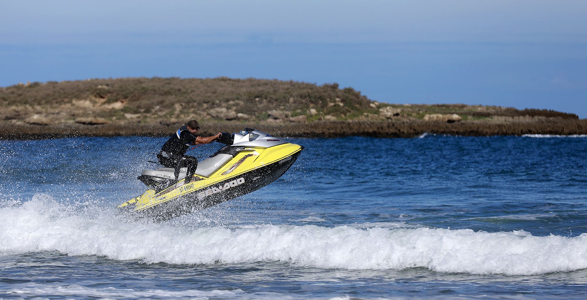 A person jet-skiing on a water body with a rocky shoreline in the background.