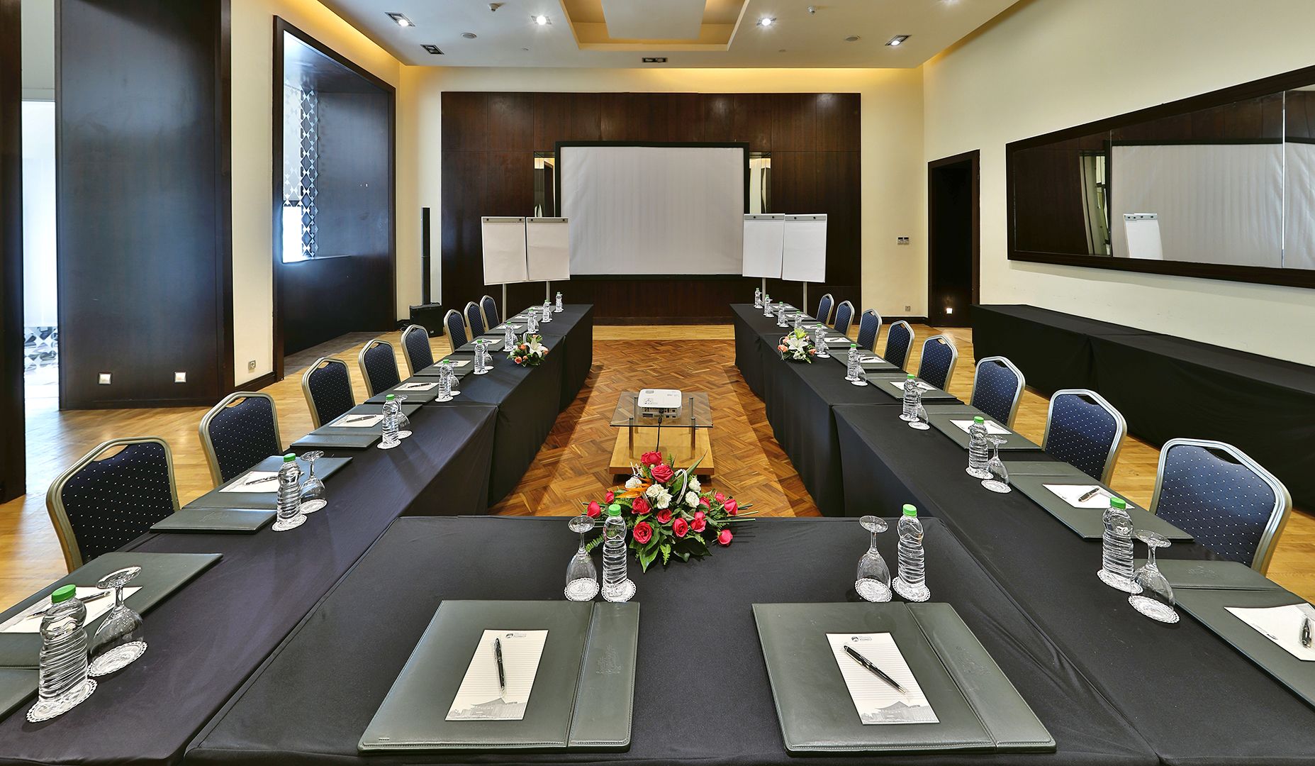 A conference room with a long table, chairs, and a projector screen.