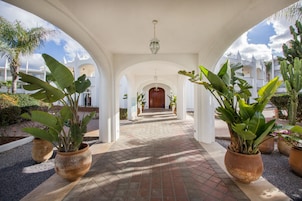 Uma galeria coberta com plantas em vasos e uma porta de madeira no final.