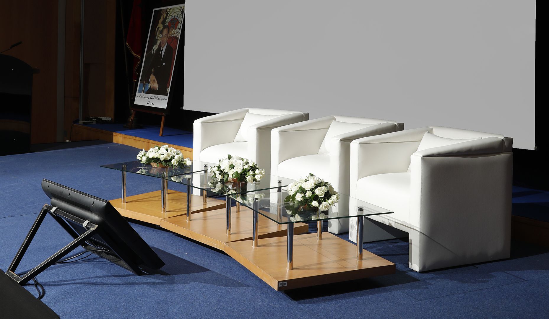 A modern conference room with three white leather sofas arranged around a glass table, each with a vase of white flowers.