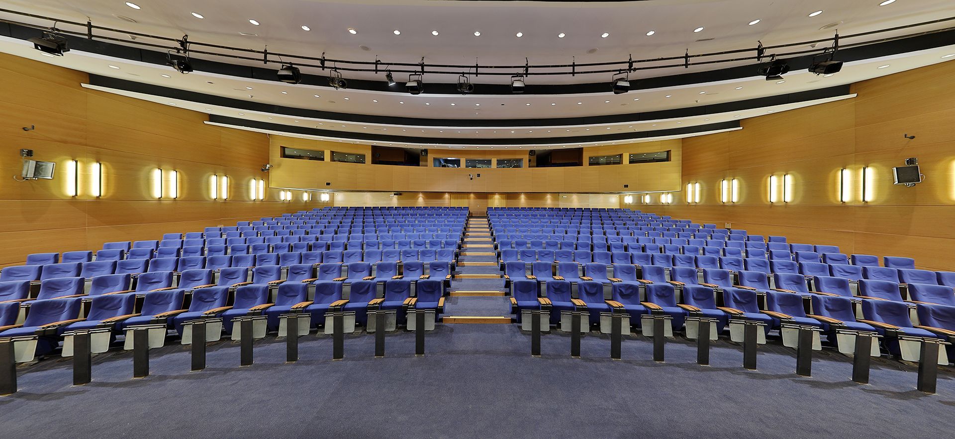Un auditorio amplio y vacío con filas de sillas azules y un escenario al frente.