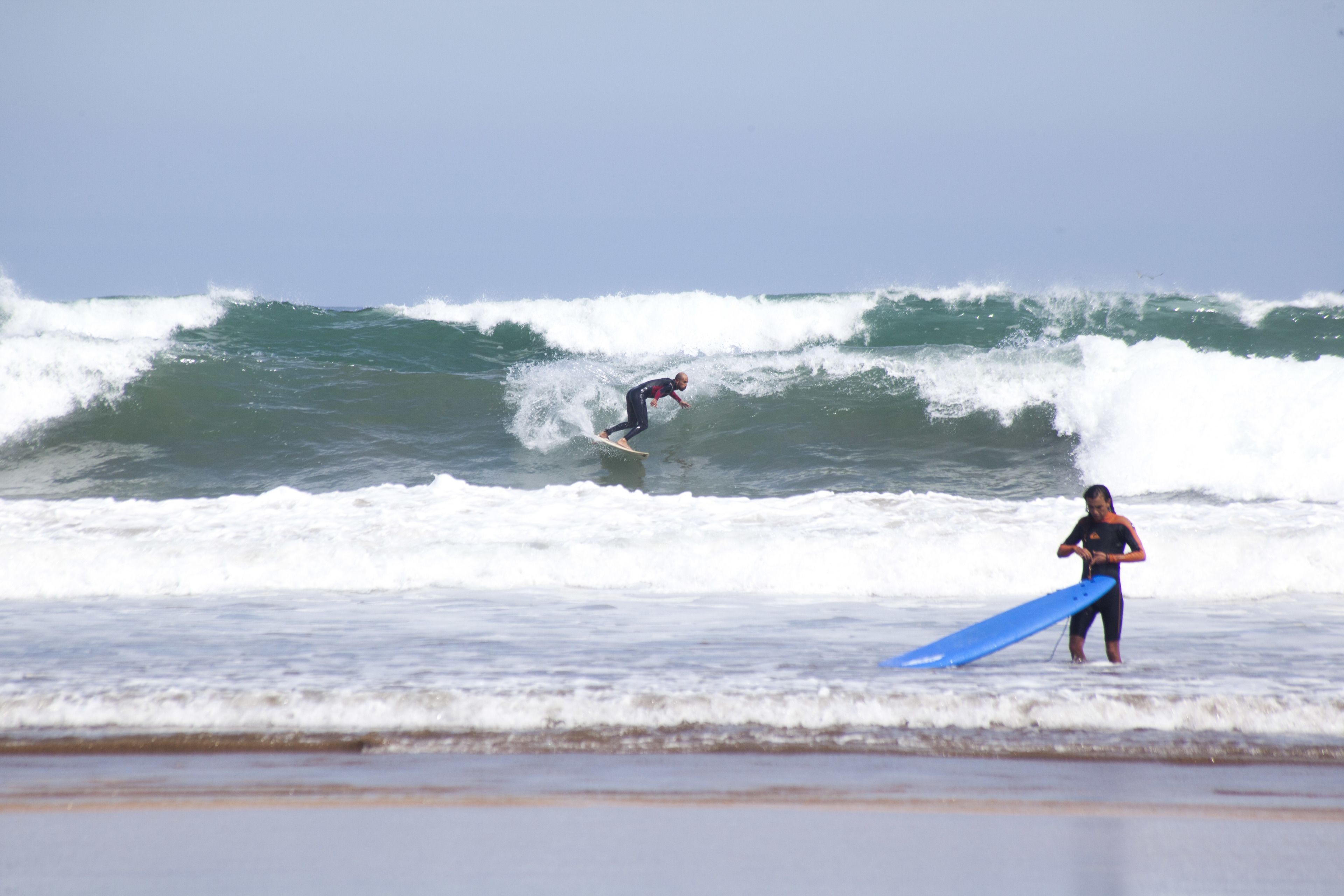 Une scène de plage où l'on voit un surfeur chevauchant une vague et une autre personne tenant une planche de surf.
