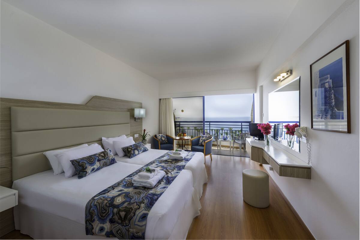 Une chambre d’hôtel avec un grand lit, un balcon avec vue, un bureau et une chaise.