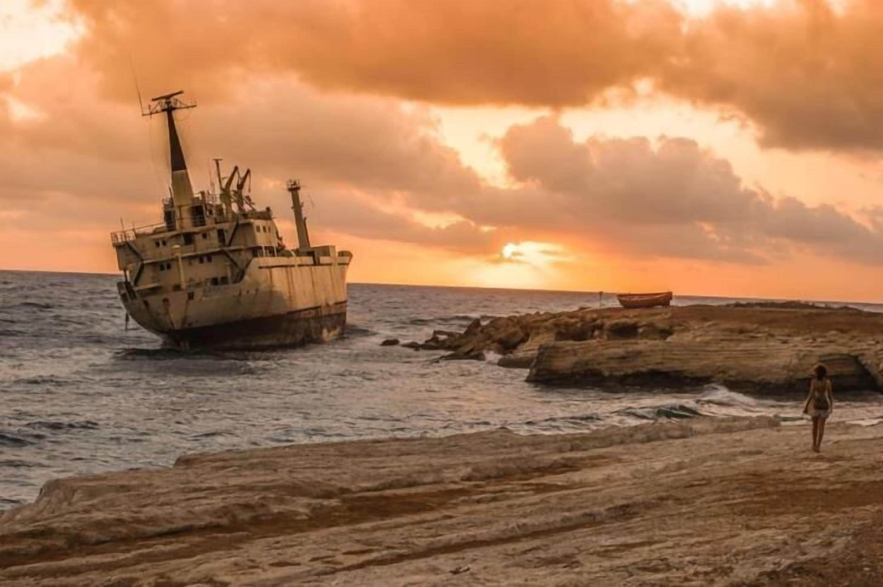 Un navire échoué sur une côte rocheuse, avec un coucher de soleil en arrière-plan.