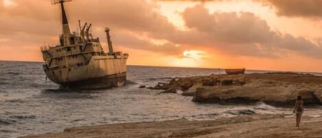 A shipwreck on a rocky shore with a sunset in the background.