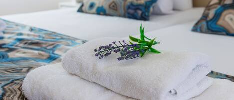 A neatly made bed with white linens and decorative pillows, a small plant on the side, and a patterned bedspread.
