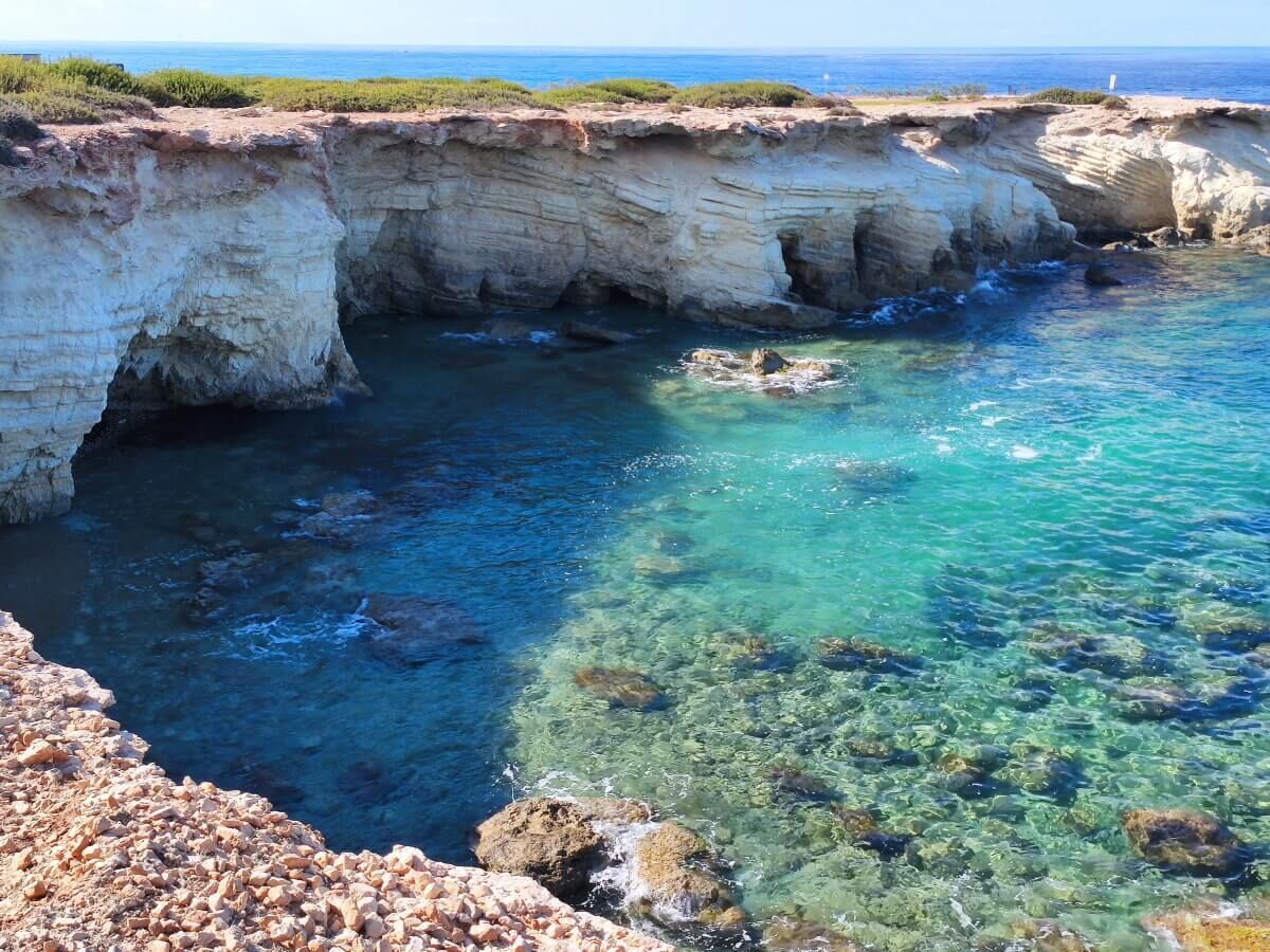 Un acantilado costero con aguas azul turquesa y terreno rocoso.