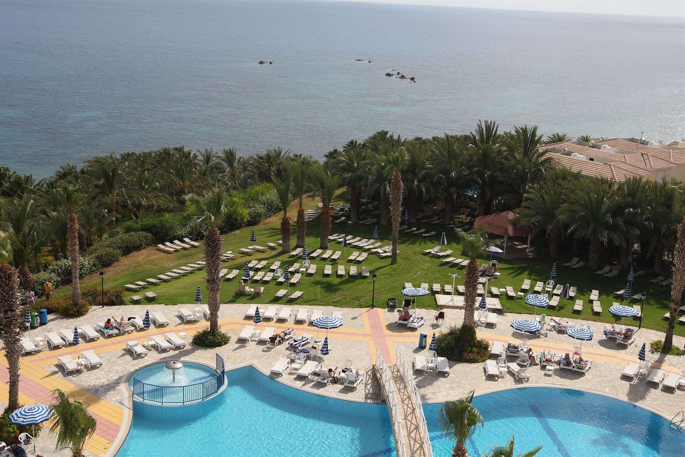 Un resort con piscina, sillones de descanso, sombrillas y vistas al mar.
