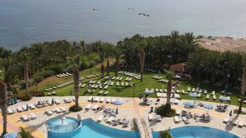 Un resort con piscina, sillones de descanso, sombrillas y vistas al mar.