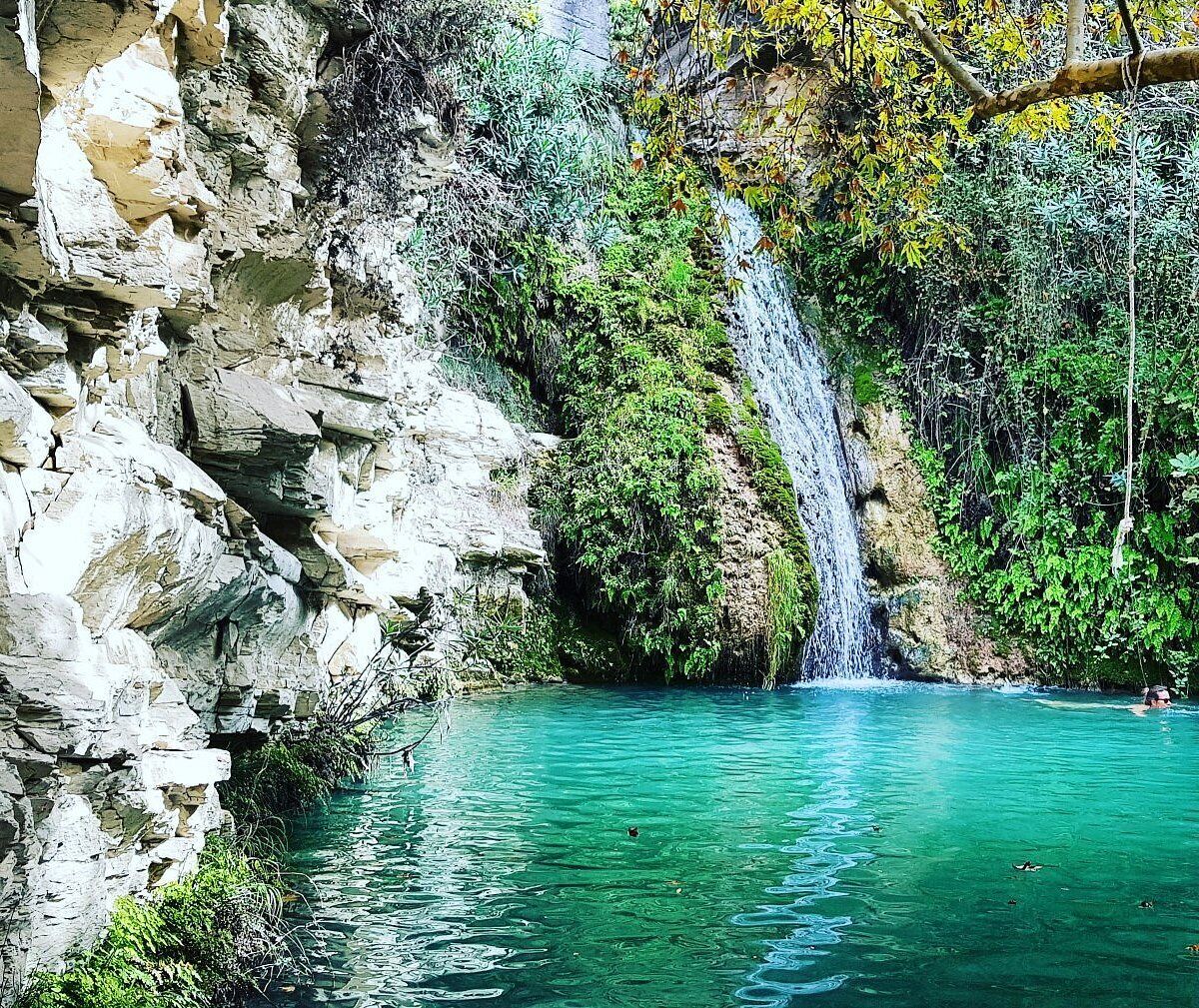 Una piscina natural de agua turquesa cristalina, rodeada de acantilados rocosos y exuberante vegetación.