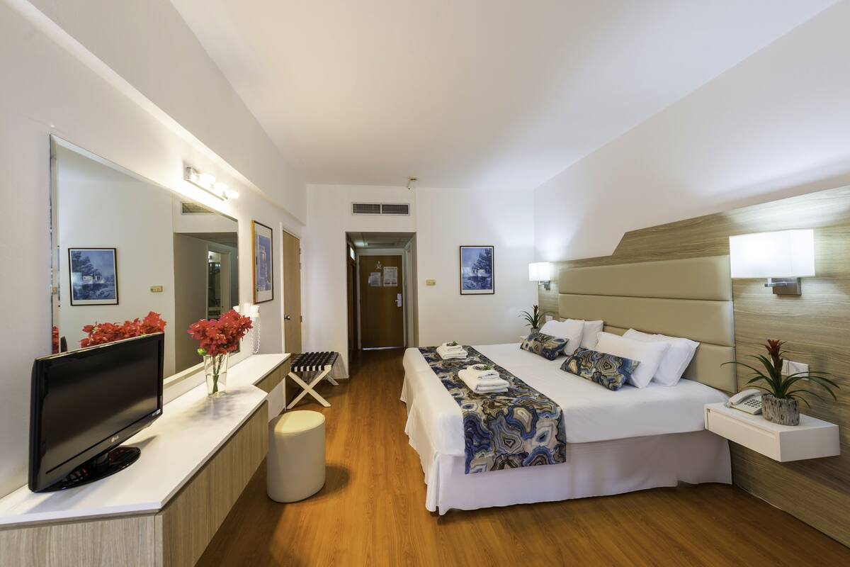 Une chambre d’hôtel moderne dotée d’un grand lit, d’une télévision à écran plat, d’un bureau avec un ordinateur et d’un miroir.