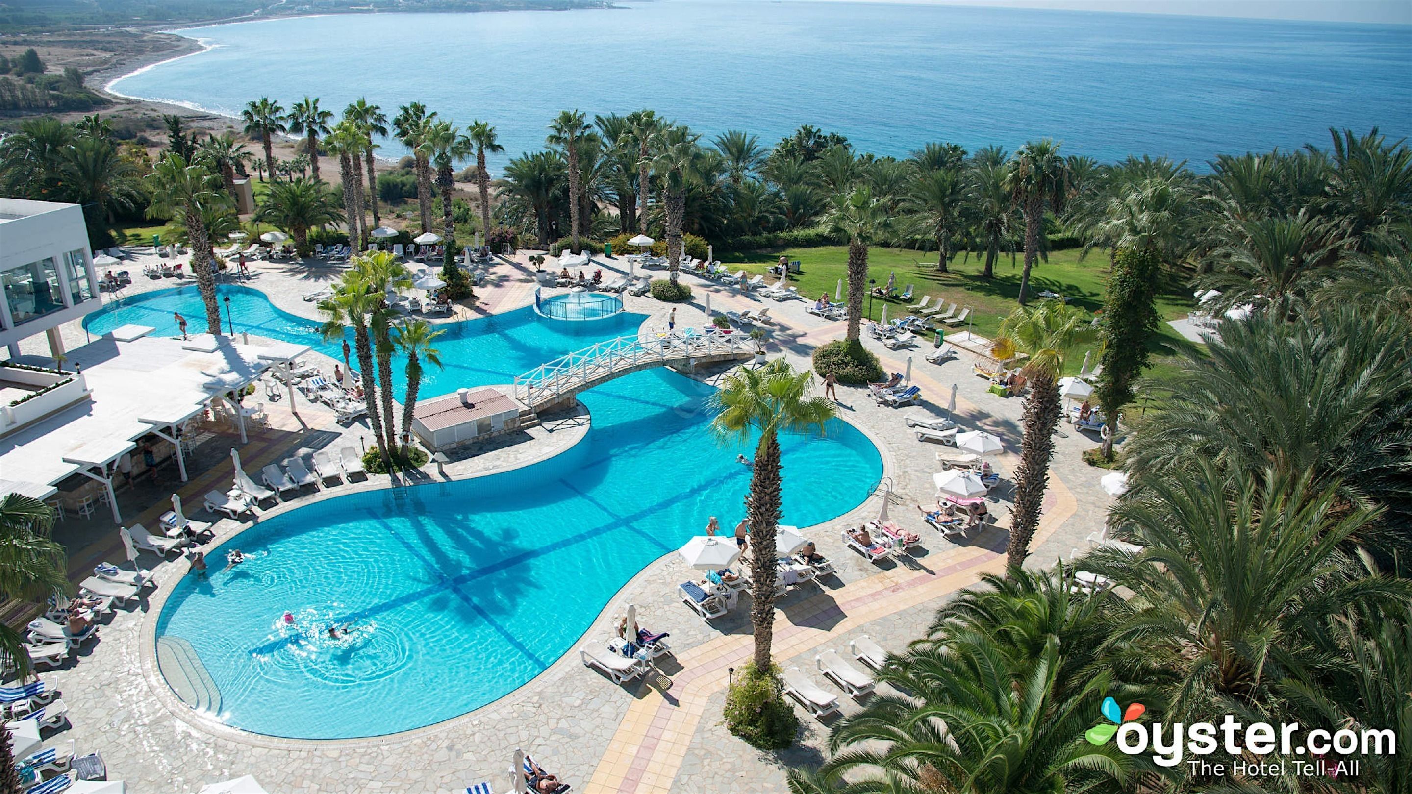 Un resort con varias piscinas, palmeras y vista al océano.
