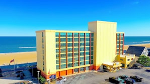 Un hotel amarillo con una amplia fachada de vidrio, situado cerca de una playa bajo un cielo azul cristalino.