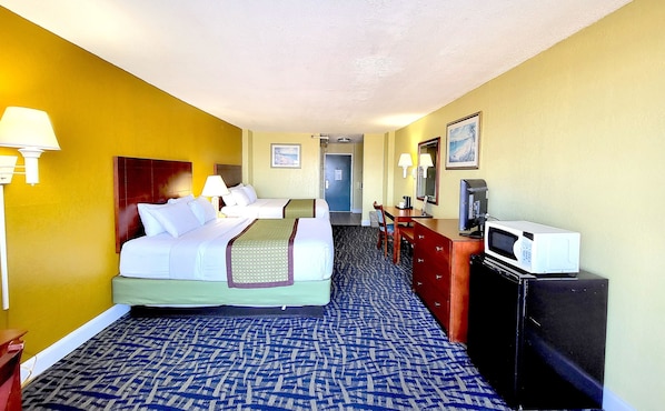 Una habitación de hotel con una cama, lámparas de noche, un escritorio con una computadora, un microondas y un televisor.