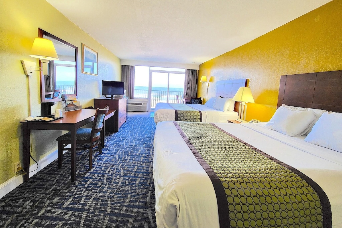 Habitación de hotel con cama, escritorio, silla, televisión y vista al océano.