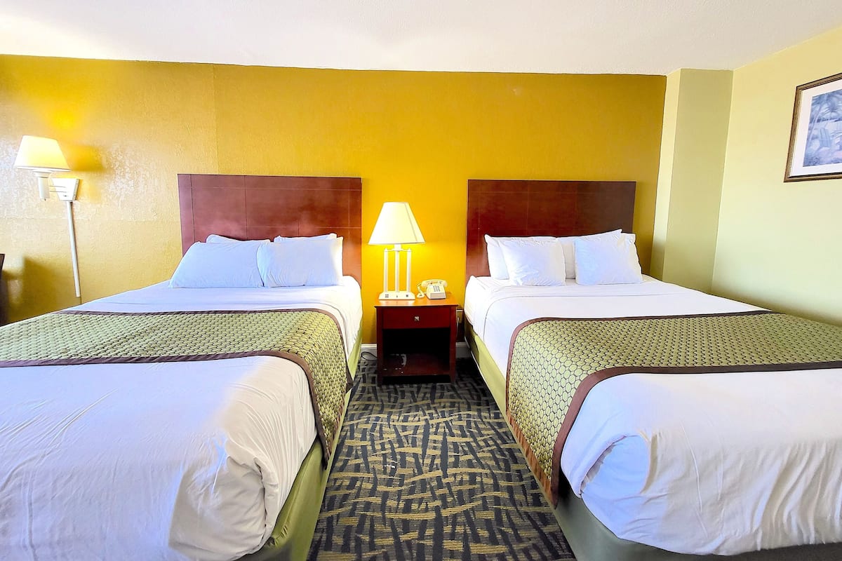 A hotel room with two beds, a nightstand with a lamp, and a framed picture on the wall.