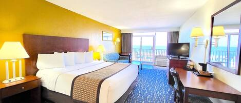 A hotel room with a large bed, two bedside lamps, a desk with a chair, a television, and a view of the ocean through the balcony doors.