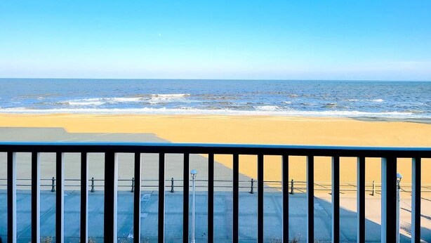 Vista de la playa desde un balcón con barandilla, mar y cielo despejado.